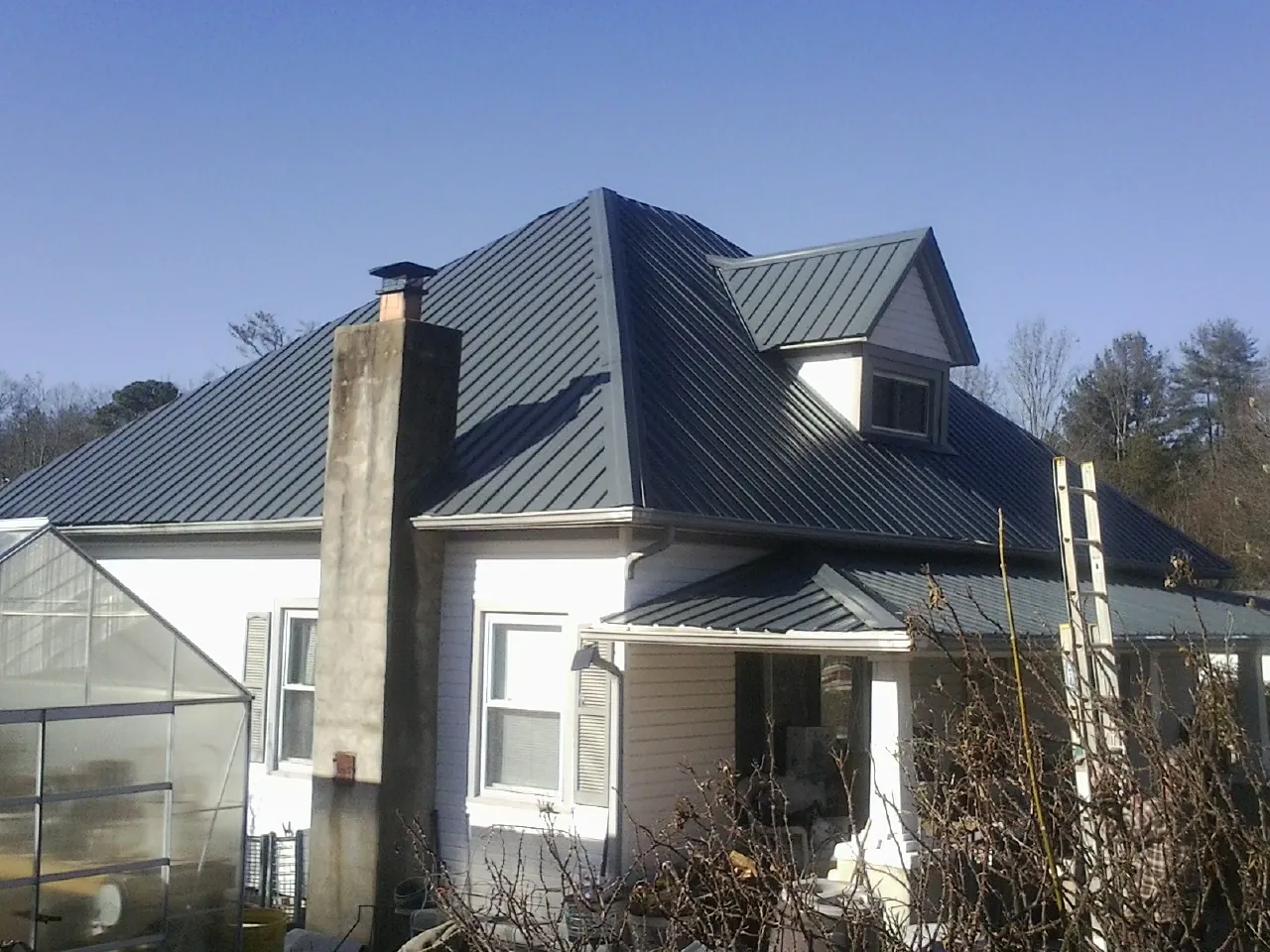 Dark blue standing seam metal roof on a white farmhouse with dormer — Slate & Tile Roof Repair by Roofing Brothers in Whiteside