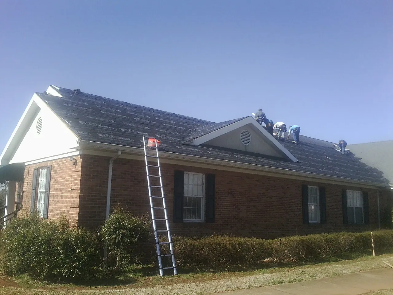 Crew tearing shingles off a brick ranch roof with a ladder set — Metal Roof Repair work by our crew in Whiteside