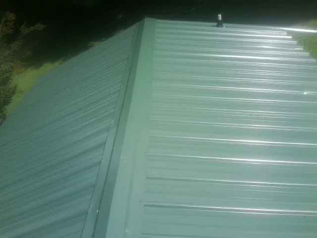 New green metal panels meeting at the ridge of a roof — Flat Roof Repair work by our crew in Whiteside