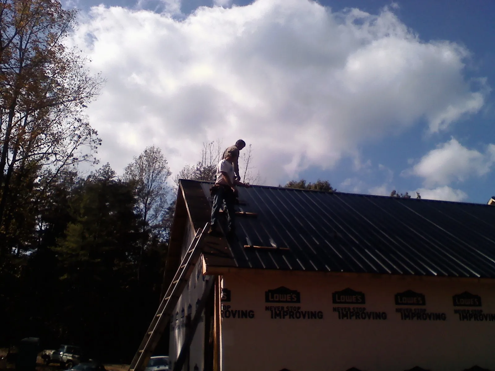Roofer fastening dark metal panels high against a cloudy sky, from a Roof Inspection job in Whiteside