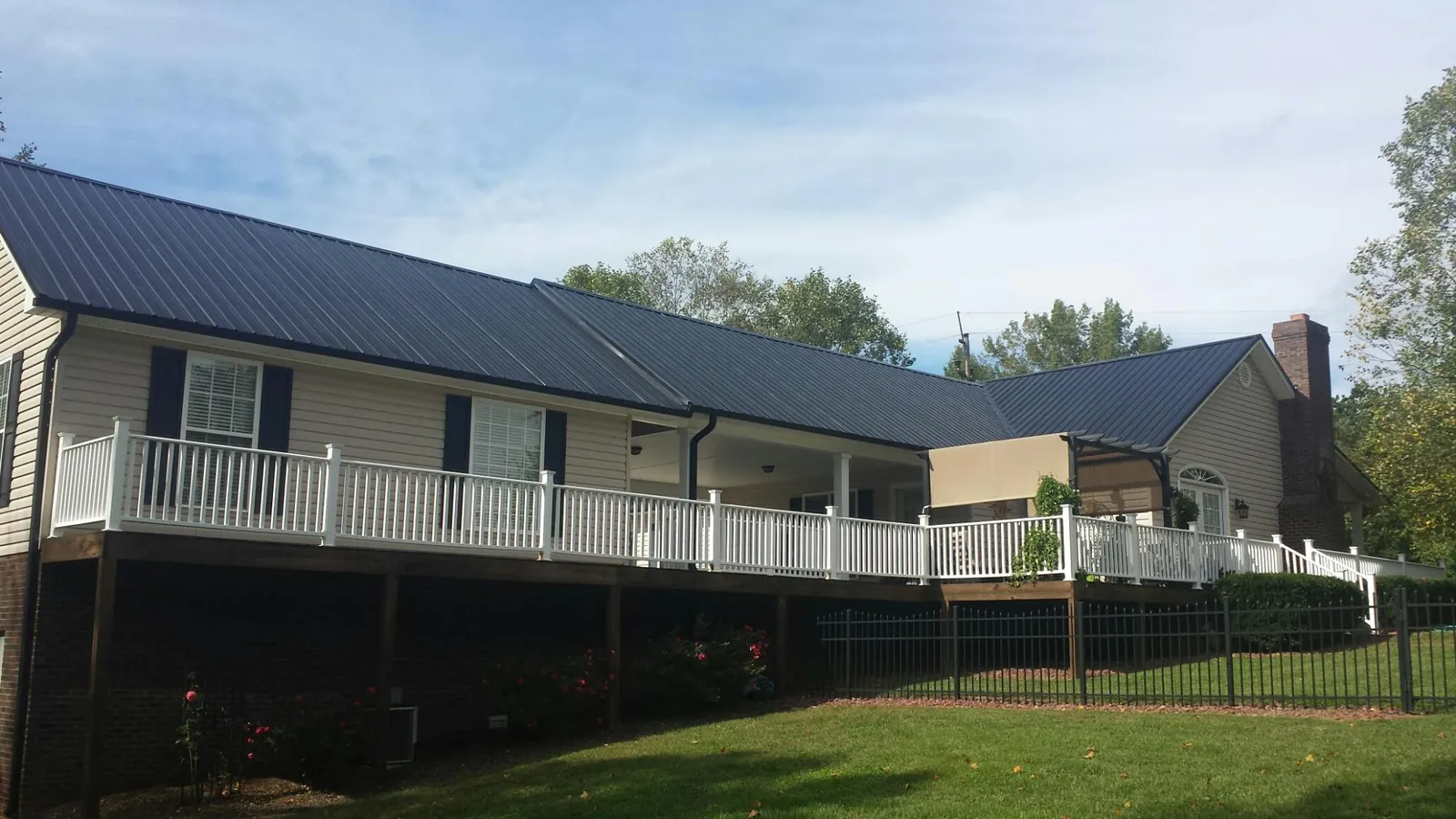 Black metal roof above a long white railed deck on a hillside home in Whiteside