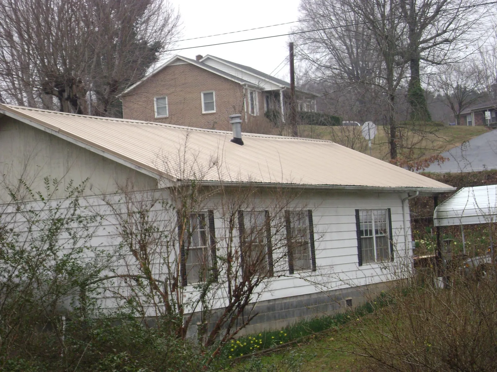 Tan metal roof on a white sided house set into a hillside — Commercial Roofing by Roofing Brothers in Whiteside